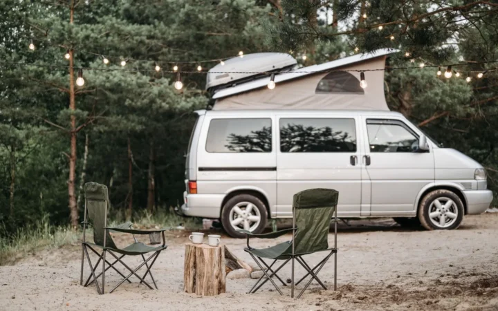 Camper van at a wooded campsite with chairs and string lights