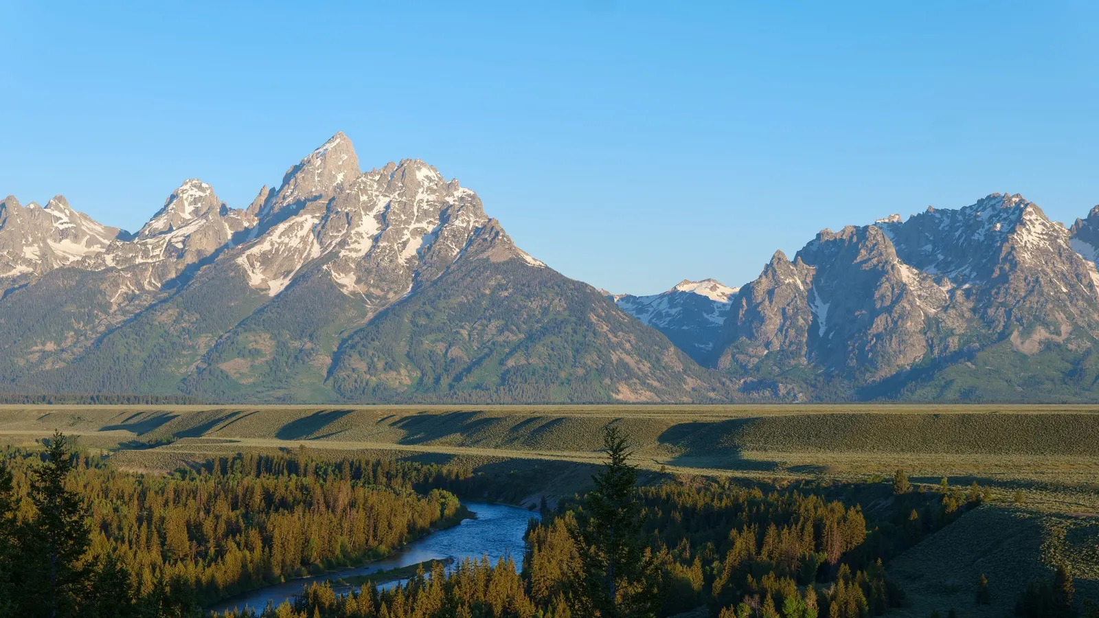 The Teton Range rising above forest and a winding river valley