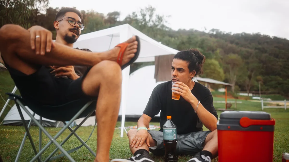 Two friends relaxing at a campsite beside a red cooler
