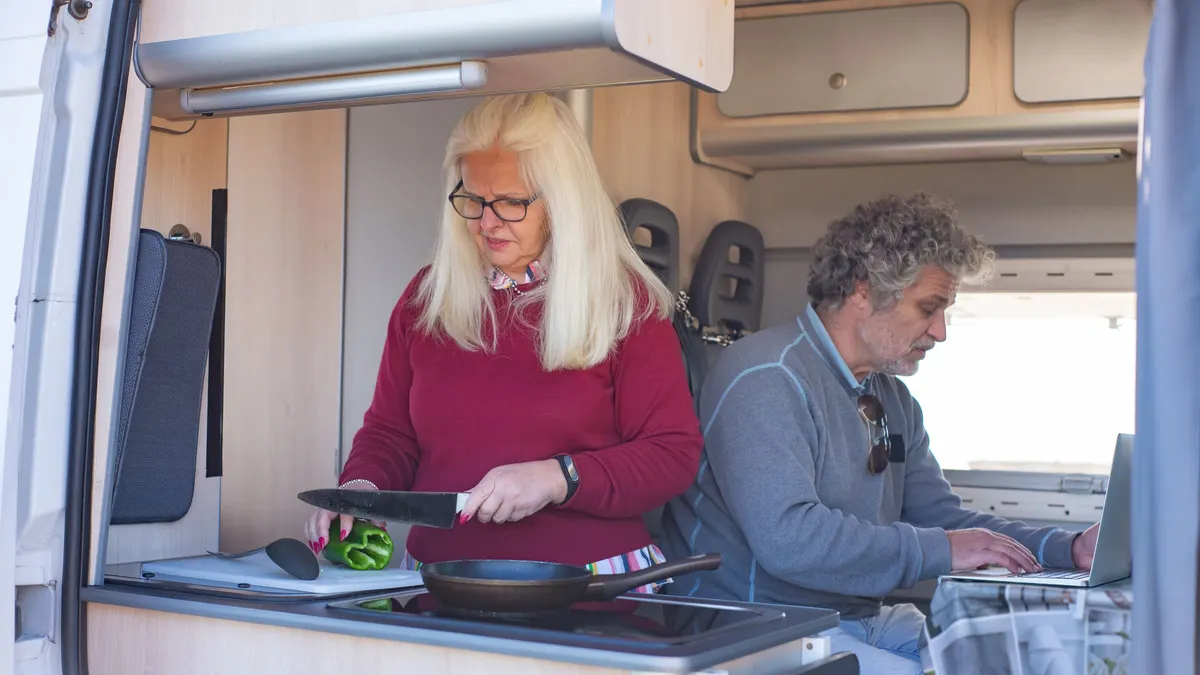 Two people working on laptops at the table inside a camper van