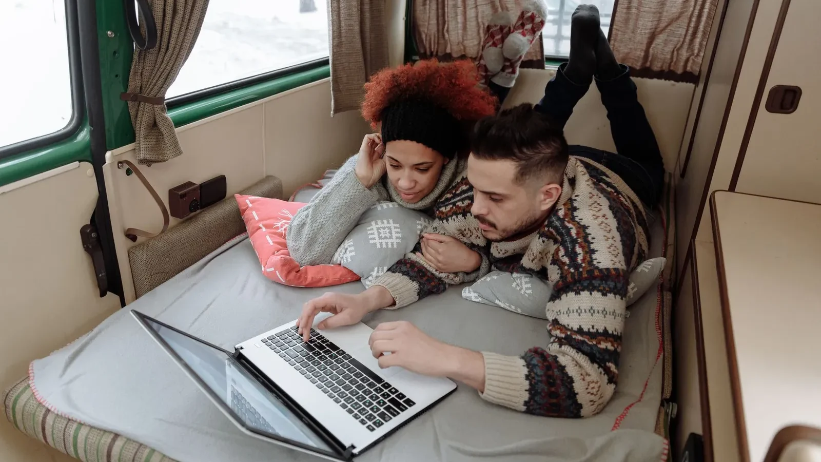 Couple lying in a camper van bed using a laptop to stay connected on the road