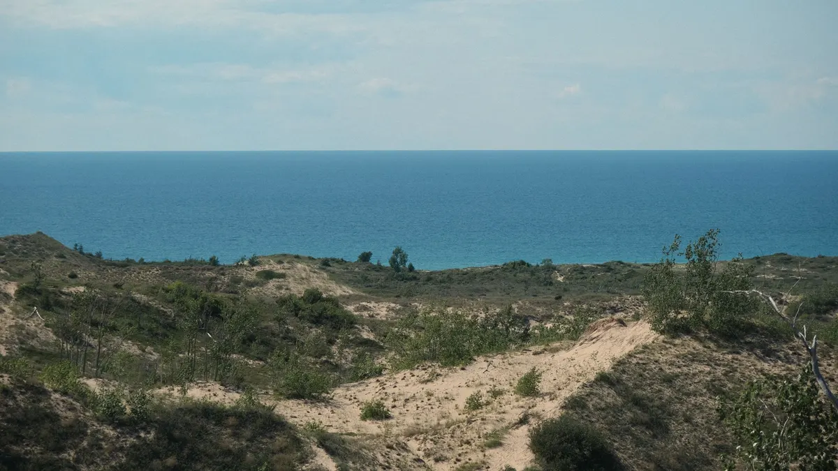 Grassy dunes above deep blue lake water stretching to the horizon