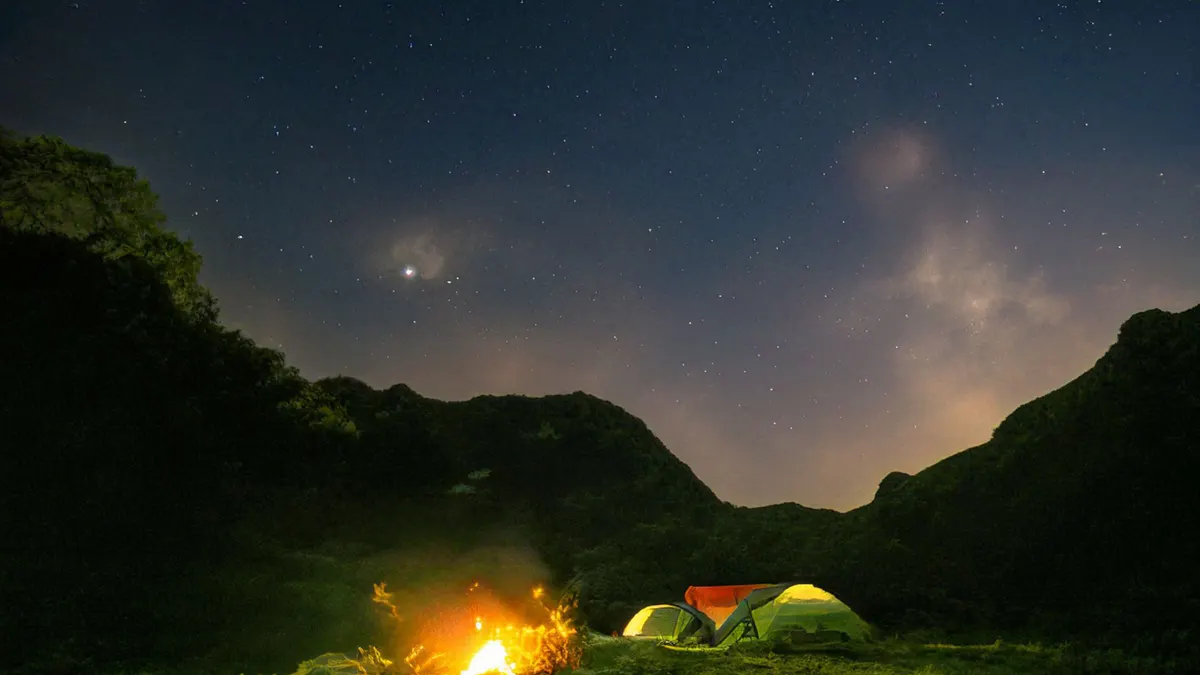 Small tents and a campfire glowing in a mountain valley under a night sky