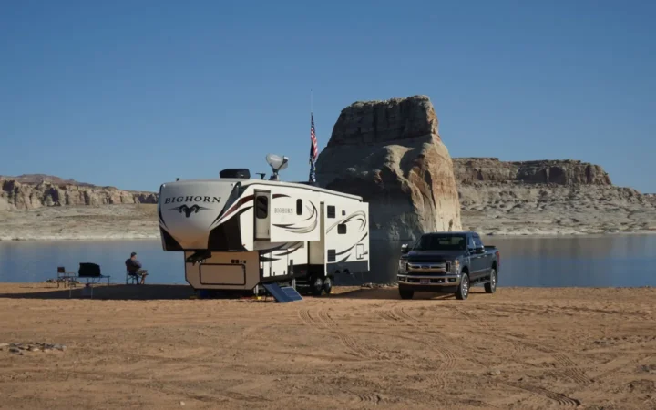 Travel trailer and truck parked on an open desert lakeshore with a rock formation behind