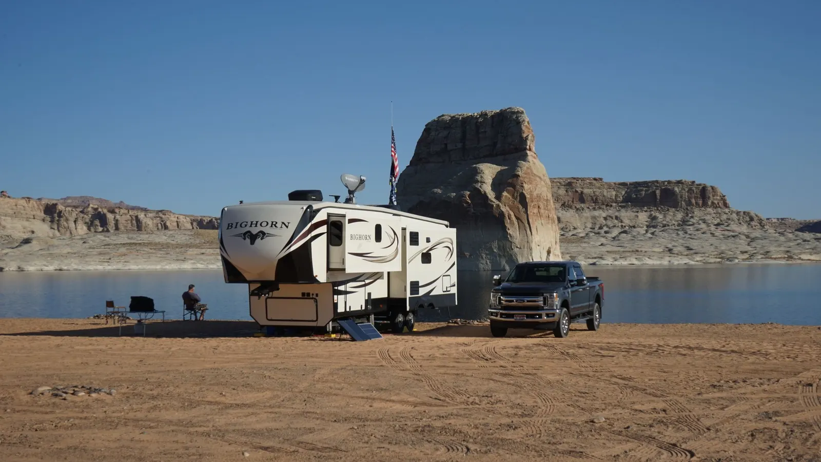 Travel trailer and truck parked on an open desert lakeshore with a rock formation behind