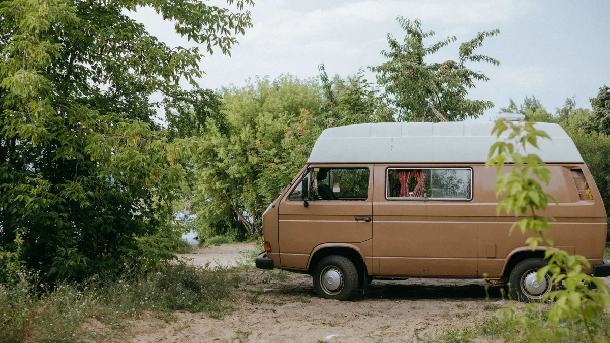 Vintage camper van parked beside a dirt forest road