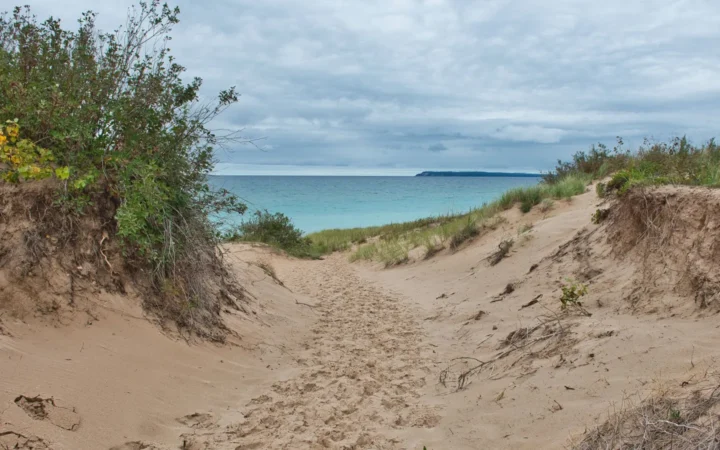 Sandy dune trail leading down to a blue Great Lakes shoreline