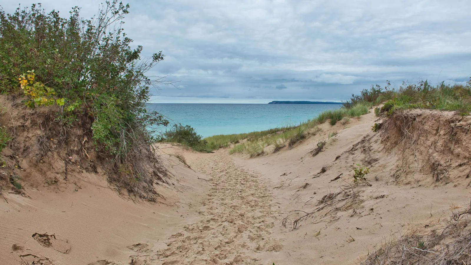 Sandy dune trail leading down to a blue Great Lakes shoreline