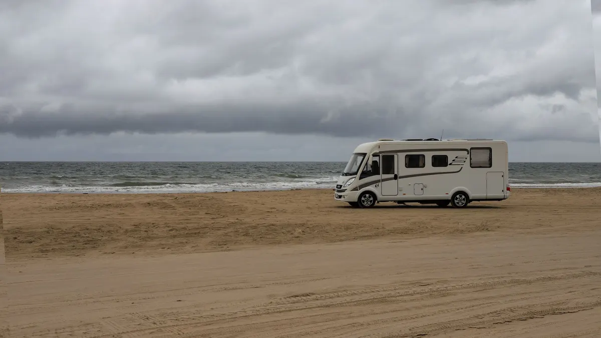 Motorhome parked alone on a wide sandy beach under grey skies