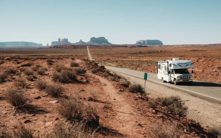 Motorhome driving a desert highway with red rock buttes on the horizon