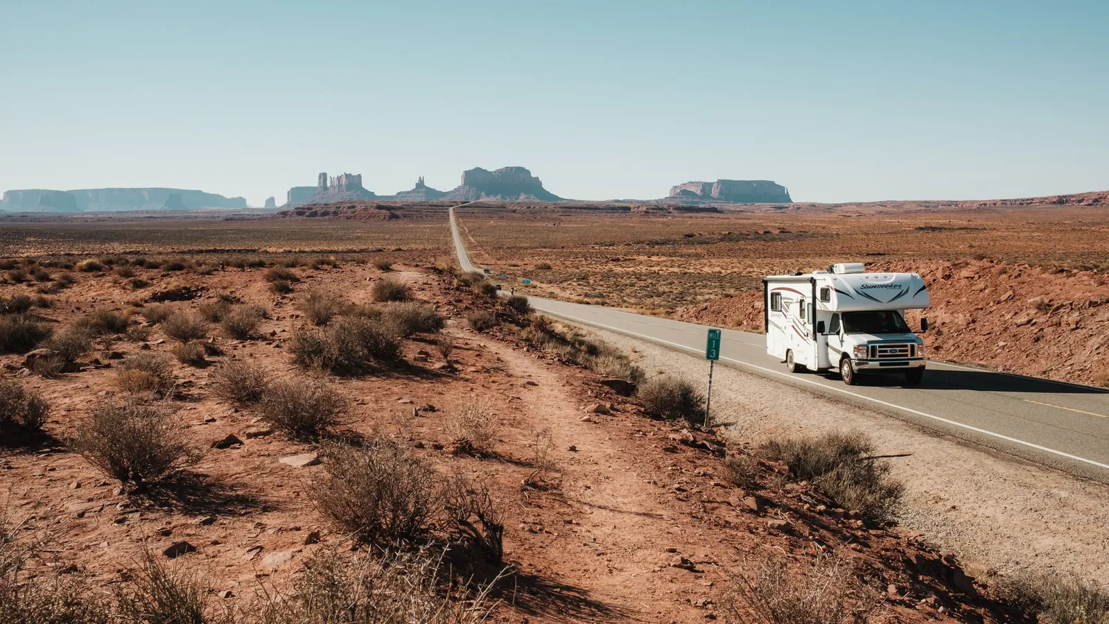 Motorhome driving a desert highway with red rock buttes on the horizon