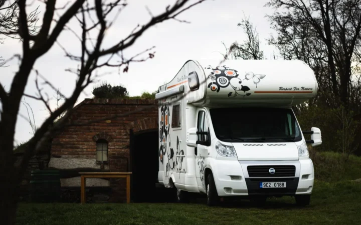 White Class C motorhome parked at a grassy campsite beside a tree