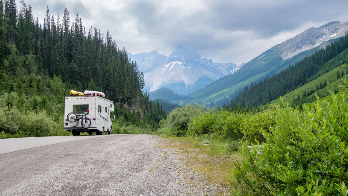 RV parked on a gravel road in a green mountain valley with snowy peaks