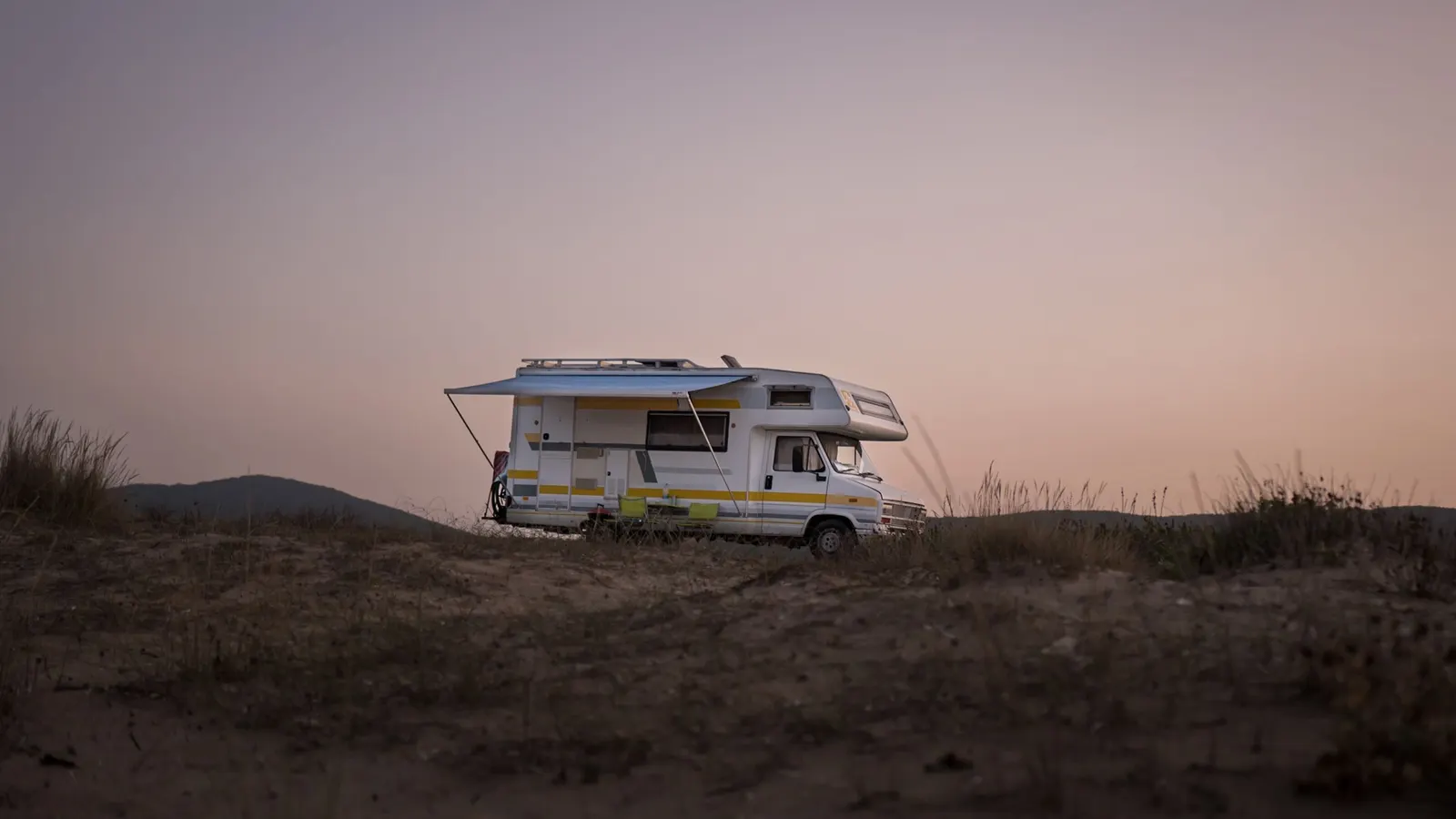Class C motorhome parked on open ground at dusk