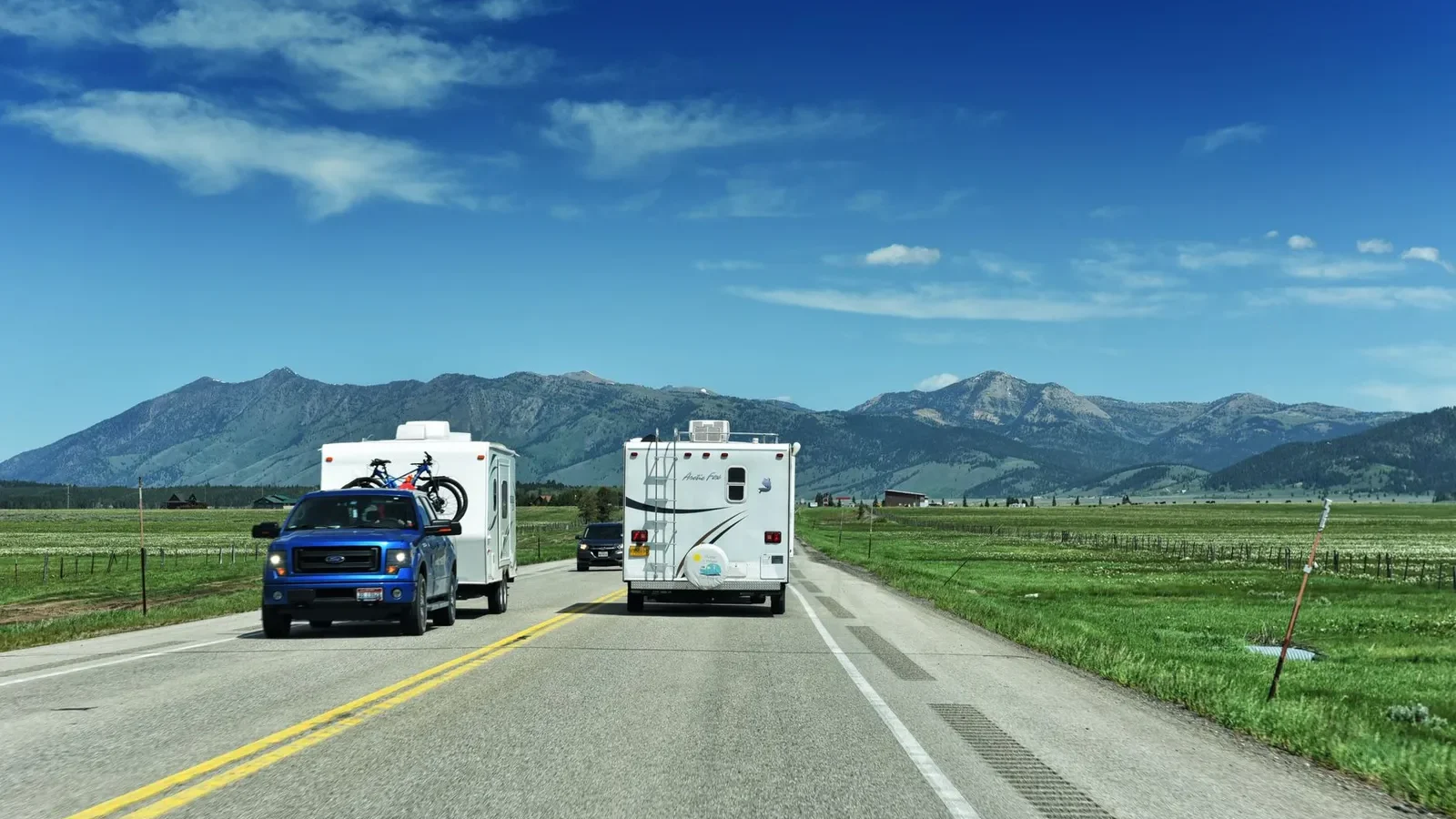 Pickup towing a travel trailer and a motorhome driving an open highway through a mountain valley