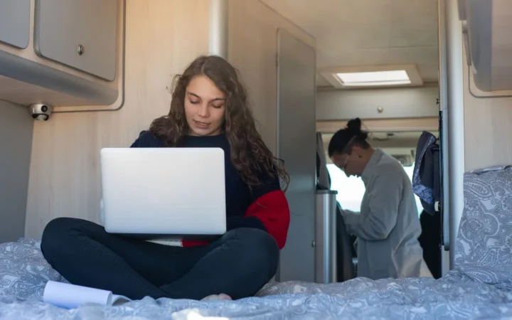 Woman working on a laptop while sitting cross-legged inside a camper