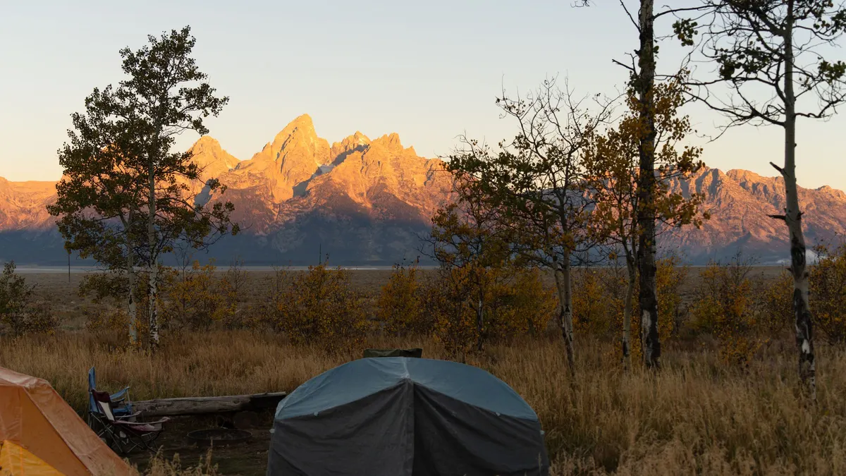 Tent at a campsite with jagged mountain peaks glowing at sunrise