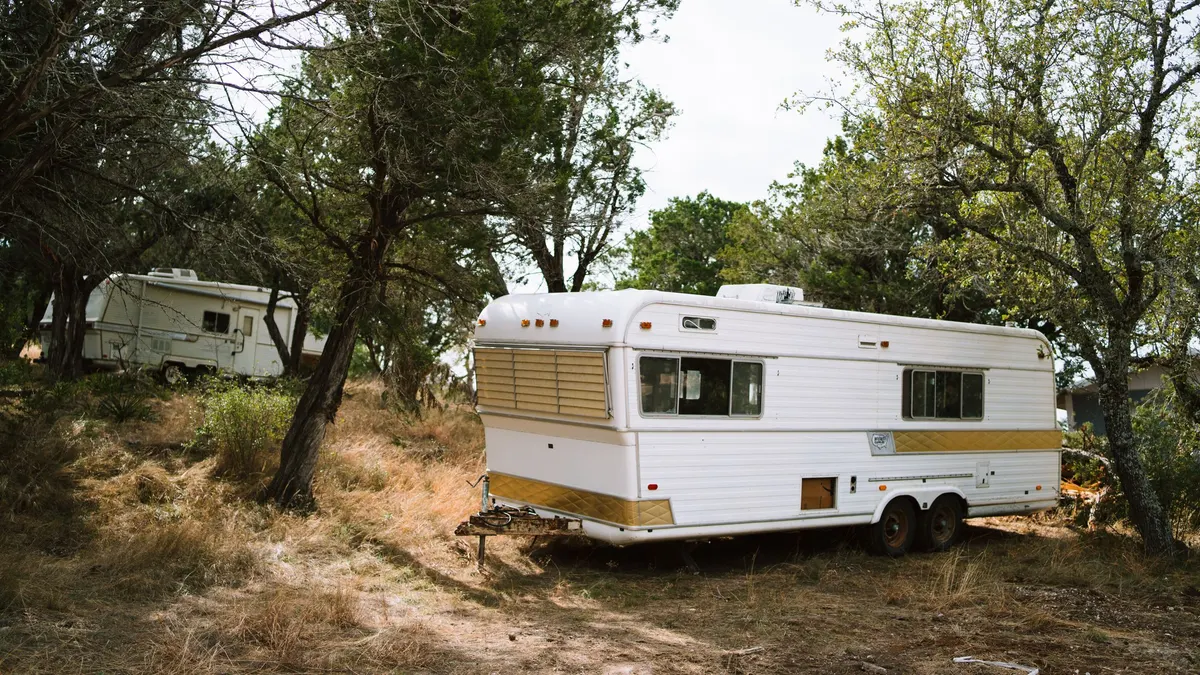 Travel trailer parked in a wooded campsite among tall trees
