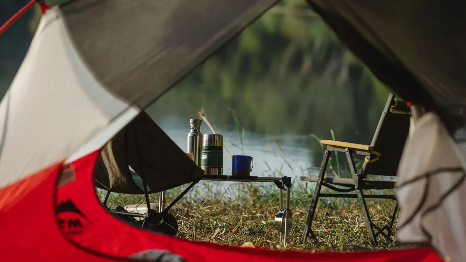 View from inside a tent of camp chairs and a small table beside a lake