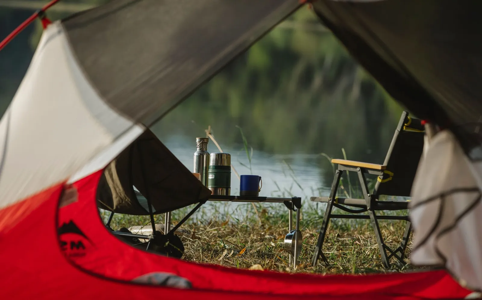 View from a tent of camp chairs beside a lake