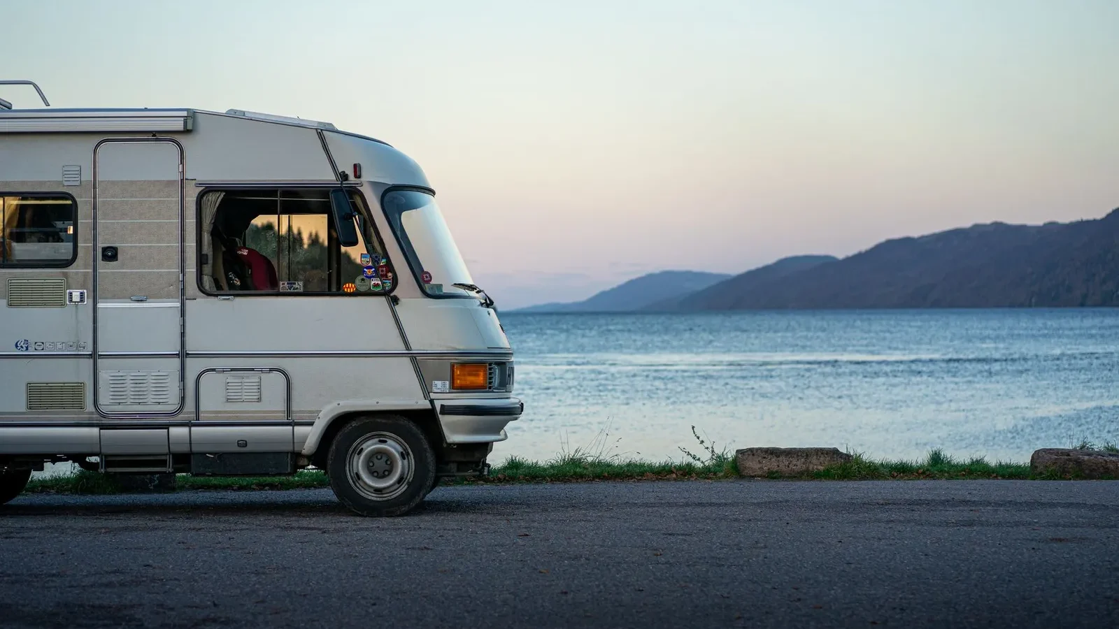 Vintage camper parked beside a calm lake at dusk