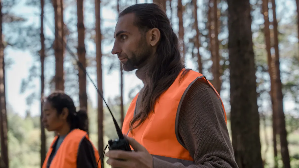 Two people in orange safety vests working in a forest
