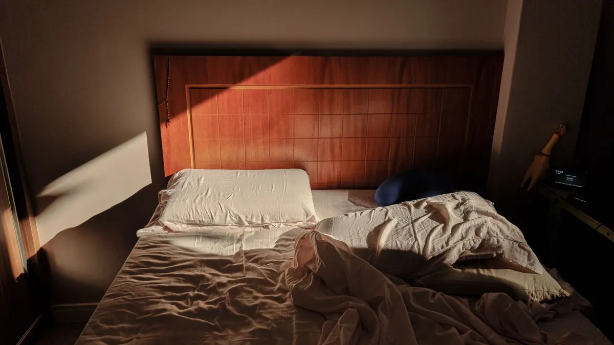 Unmade bed with a wooden headboard in soft light