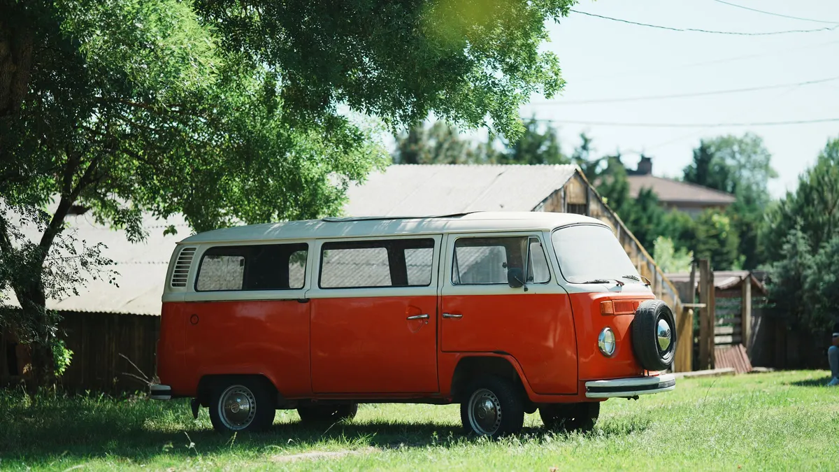 Orange and white camper van parked on grass in the shade of trees