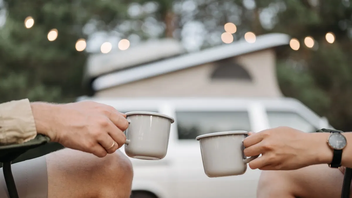 Two people toasting enamel mugs at a campsite