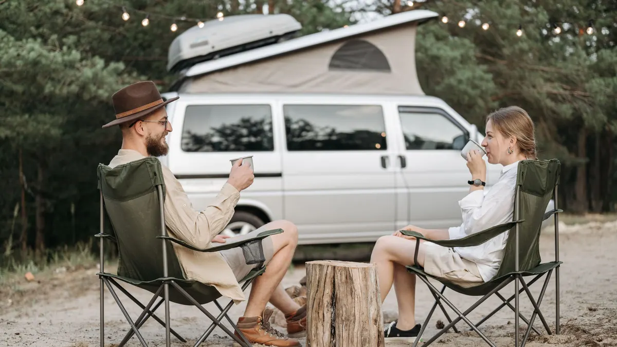 Two people sitting in camp chairs beside a white van