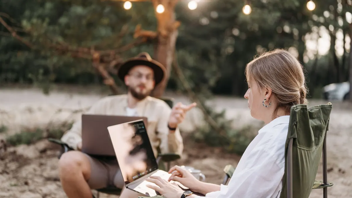 Two people working on laptops at a campsite