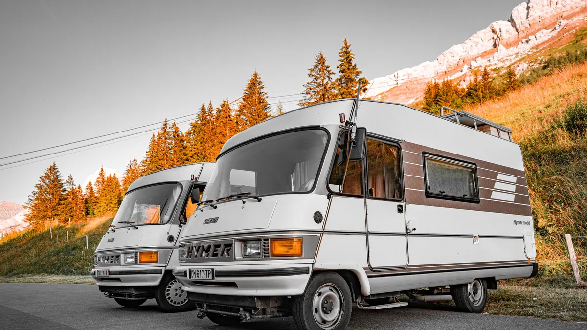 Two older Class C motorhomes parked on a roadside pull-out in evening light