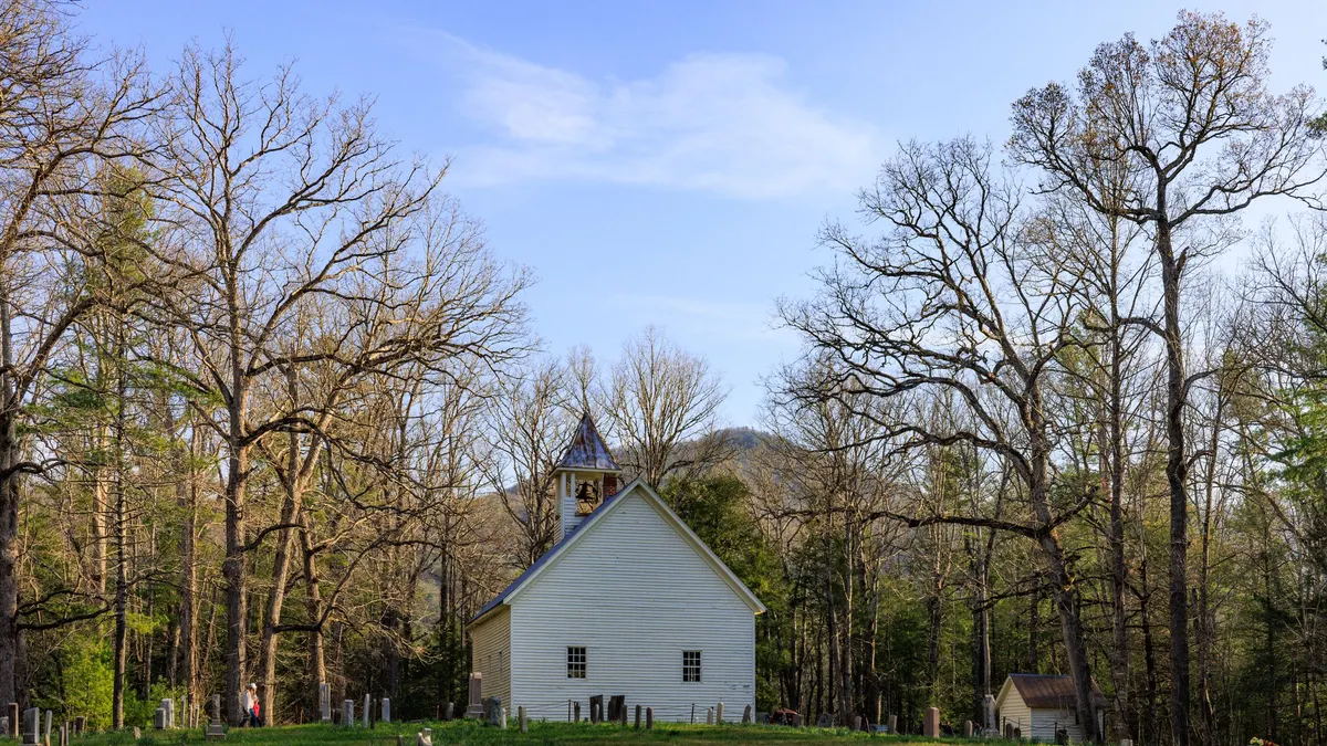 Historic white church in a grassy valley surrounded by bare trees