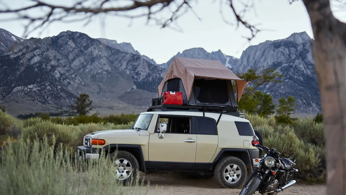 SUV with a rooftop tent camped below rugged mountains