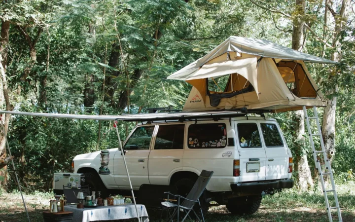 Overland camp with a rooftop tent, awning, chairs and a camp kitchen set up beside an SUV