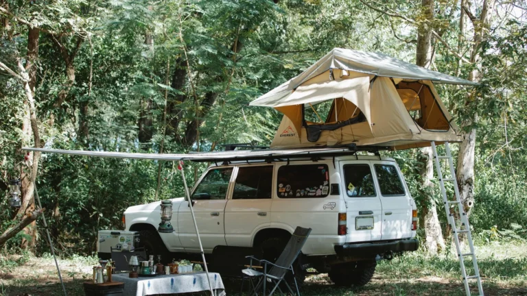Overland camp with a rooftop tent, awning, chairs and a camp kitchen set up beside an SUV