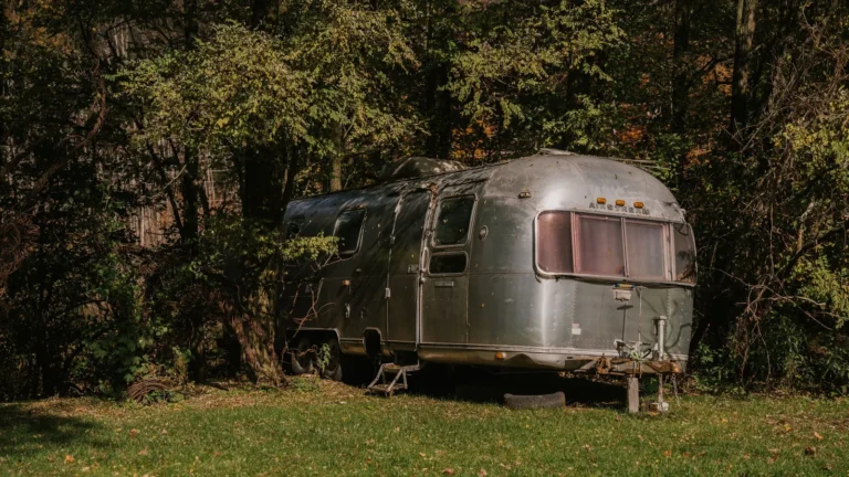 Silver travel trailer parked at a wooded campsite