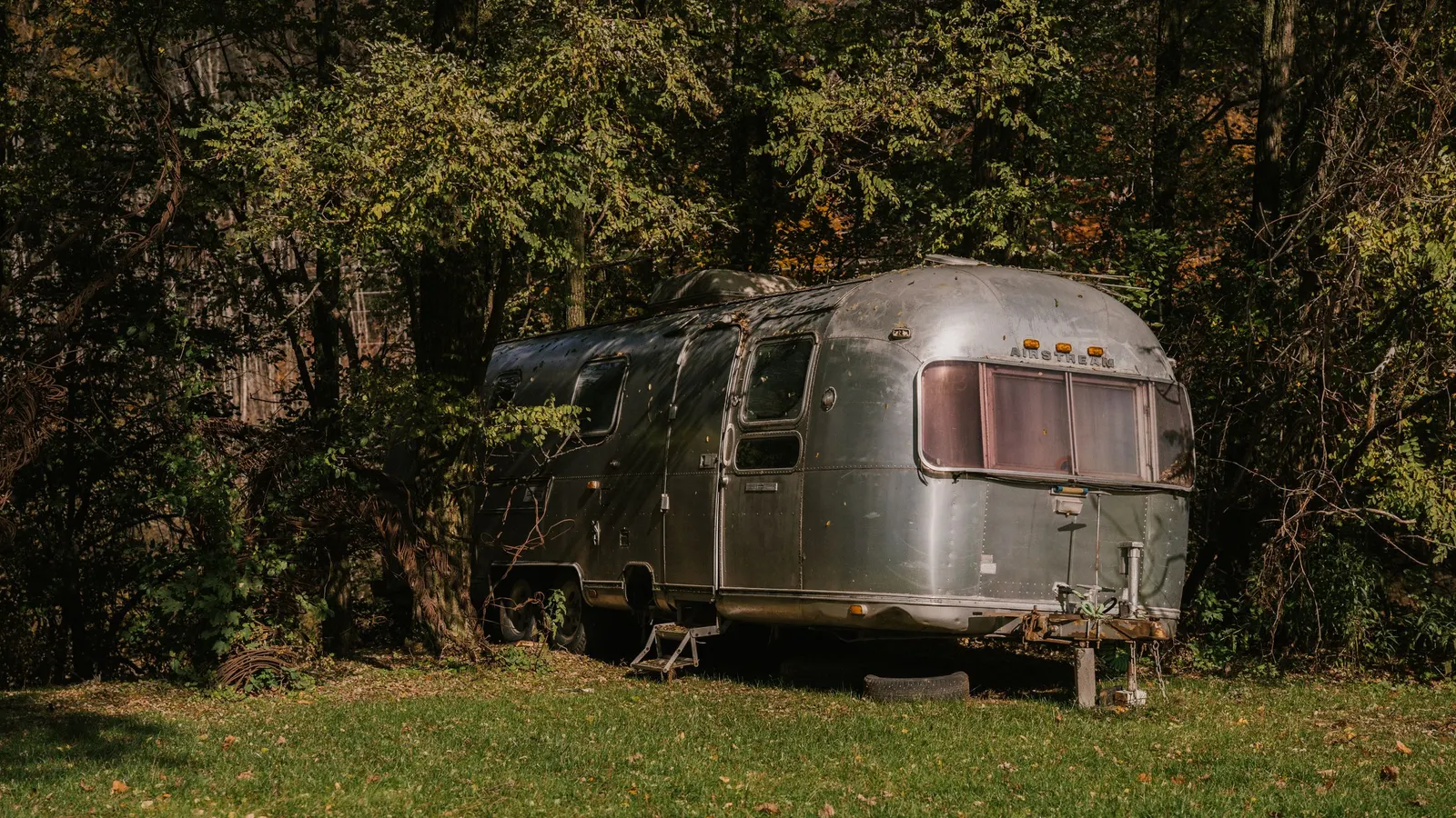 Silver travel trailer parked at a wooded campsite