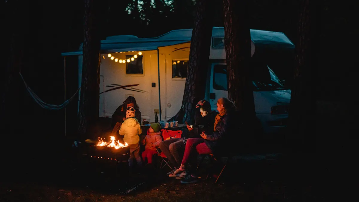 Travelers around a campfire beside a camper at dusk