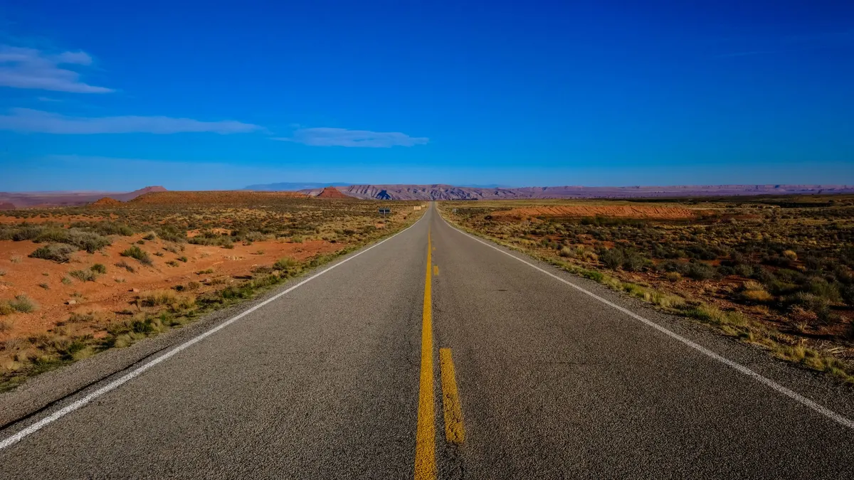 Straight desert highway leading toward mesas under blue sky