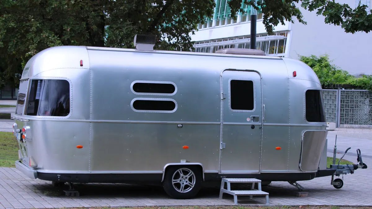 Silver travel trailer parked on grass with entry steps down