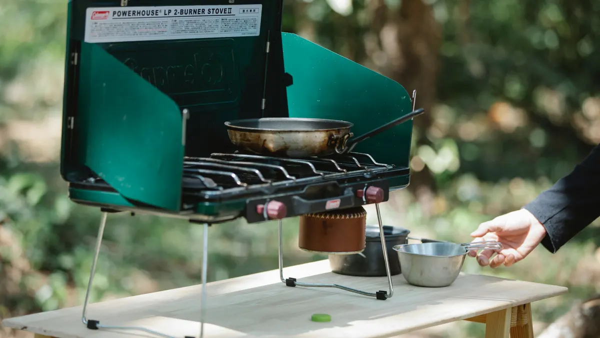 Two-burner propane camp stove with a pan cooking outdoors
